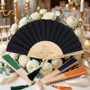 Peut inclure: Éventails de mariage noirs et en bois gravés des noms "AYA & GEORGE" et de la date "02.10.2026". Les éventails portent le message "Thank you for celebrating with us!" et sont présentés avec des roses blanches.