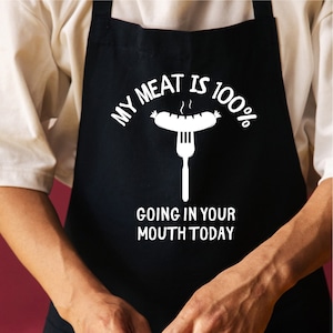 May include: A black apron with the text "My meat is 100% going in your mouth today" and a white illustration of a sausage on a fork.