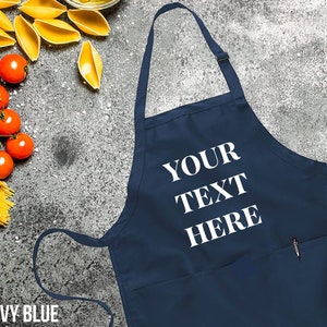 May include: Navy blue apron with a large white pocket and the text "YOUR TEXT HERE" printed on the front.