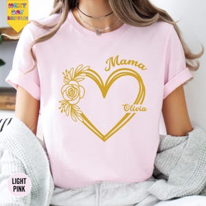 A woman wearing a pink t-shirt with a heart design and the names "Mama" and "Olivia" printed on it.