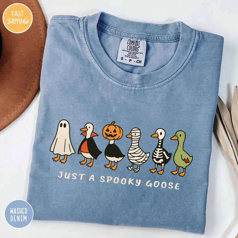 A blue t-shirt with a graphic design of a skeleton goose and a ghost, along with the text "Just a Spooky Goose" printed on it.