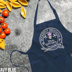 May include: Navy blue kitchen apron with a white design that says "Wickedly Delicious Witch's Kitchen Stirring Up Some Magic".