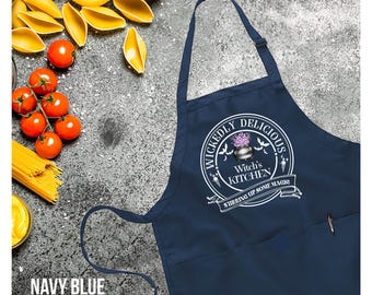May include: Navy blue apron with the text "Wickedly Delicious Witch's Kitchen" in a circular design. The apron has a pocket and adjustable neck strap. Ingredients like tomatoes, pasta, and shells are arranged around the apron.