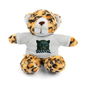 May include: A plush toy leopard with a gray t-shirt featuring a jaguar graphic and the word "DUUUVAL". The leopard has a spotted pattern in shades of tan and black. The toy has a white face and ears.