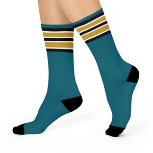 May include: Teal socks with black heels and toes. The top of the socks feature three stripes in gold, white, and black. The socks are worn on a person's feet.