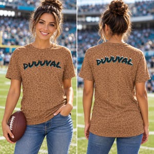 May include: A short-sleeve t-shirt with a brown leopard print pattern. The front and back feature the text DUUUVAL in a stylized font with black, white, and teal outlines. The shirt has a crew neckline and a standard fit, shown from both sides.