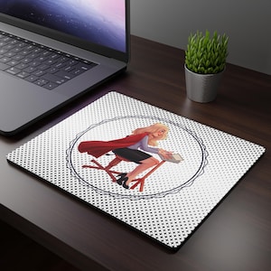 May include: White mousepad with a black and white dotted pattern and a circular illustration of a woman in a red cape riding a chair. The woman has blonde hair and is holding a book. A laptop and a small potted plant are in the background.
