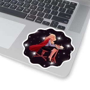 May include: A sticker featuring a blonde woman in a red cape, seated at a desk in space. The woman is wearing a gray shirt, black skirt, and heels. The background is a dark starry sky with white sparkles.