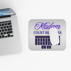 Puede incluir: Un ratón de ordenador blanco descansa sobre una alfombrilla con el texto "Madam Court Reporter" en morado y blanco. La alfombrilla tiene un fondo punteado y un gráfico morado en la parte inferior.