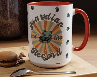 May include: White ceramic mug with a red interior and handle. The mug features the text "Guardian of the Record" with a retro typewriter graphic. The design includes a sunburst pattern in the background and small typewriter icons.