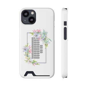 Pode incluir: Capa de telefone branca com um design floral. A capa apresenta um arranjo em estilo aquarela de flores rosa, azuis e brancas em torno de um gráfico retangular cinza. A capa tem um porta-cartões embutido e uma caixa de câmera preta.