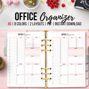Puede incluir: Un organizador de oficina rosa A5 con un archivador dorado. El organizador tiene secciones para listas de tareas, llamadas, correos electrónicos, recordatorios, proyectos, reuniones, fechas, seguimiento, notas y una sección para AM y PM. El texto "OFFICE Organizer" está impreso en la portada.