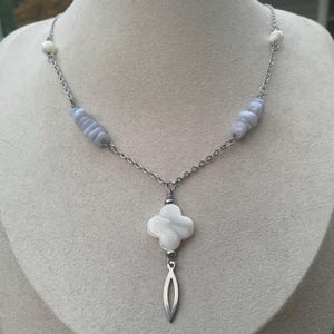 May include: A silver-toned necklace featuring a four-leaf clover pendant with a dangling teardrop shape. The necklace has a chain design with light blue and white beads.