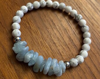 May include: A beaded bracelet featuring white and gray marble-like beads and light blue aquamarine chips. The bracelet is strung on an elastic band and includes two silver-colored metal beads.