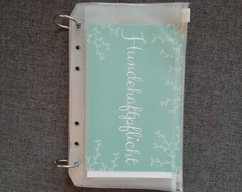 Op de afbeelding: Een transparante plastic ritszak met een witte kaart erin. De kaart heeft een lichtblauwe achtergrond met witte bloemmotieven en de tekst "Hundhaftpflicht".