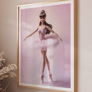 Puede incluir: Impresión enmarcada de una muñeca bailarina con tutú rosa y zapatillas de punta. La muñeca tiene el pelo castaño y posa con los brazos extendidos. El fondo es un degradado rosa suave y el marco es dorado.