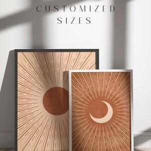 May include: Two framed prints with a sun and moon design. The sun print is in a black frame and the moon print is in a white frame. Both prints have a brown background with orange sun and moon shapes.