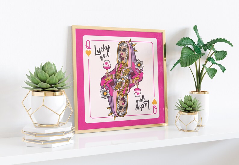 Puede incluir: Una impresi&oacute;n enmarcada de una carta de juego rosa con un dise&ntilde;o de reina de corazones. La reina lleva gafas de sol y un atuendo rosa y dorado. La carta dice "Lucky you" y "Mom's lucky charm" en letras rosa y dorado.