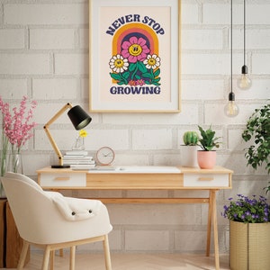 May include: A framed print with a retro-style illustration of a flower with a smiling face. The flower is surrounded by a rainbow arch and the text "NEVER STOP GROWING".