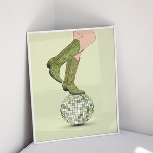 Pode incluir: Um par de botas de cowboy verdes com bordados florais em cima de uma bola de discoteca prateada sobre um fundo verde claro.