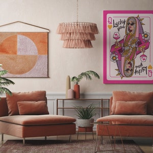 Puede incluir: Una carta de la Reina de Corazones rosa y blanca con una mujer que lleva un atuendo rosa y dorado y gafas de sol. La carta dice "Lucky You" y "moh rxpm", que es "mom" escrito al rev&eacute;s.