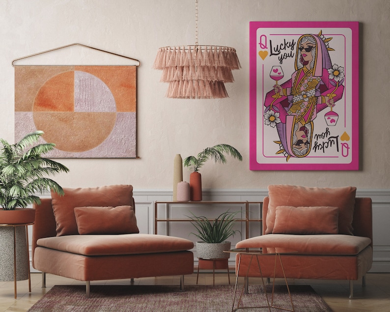 Puede incluir: Una carta de la Reina de Corazones rosa y blanca con una mujer que lleva un atuendo rosa y dorado y gafas de sol. La carta dice "Lucky You" y "moh rxpm", que es "mom" escrito al rev&eacute;s.