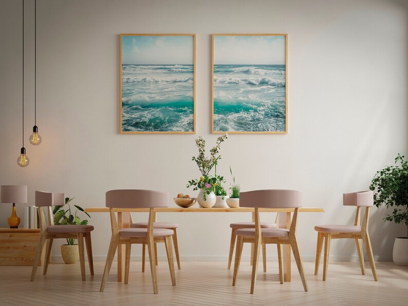 May include: A dining room scene featuring a light wood table and six chairs with pink upholstered seats. Two framed ocean wave prints hang above the table. Decorative plants and pendant lights complete the room's decor.