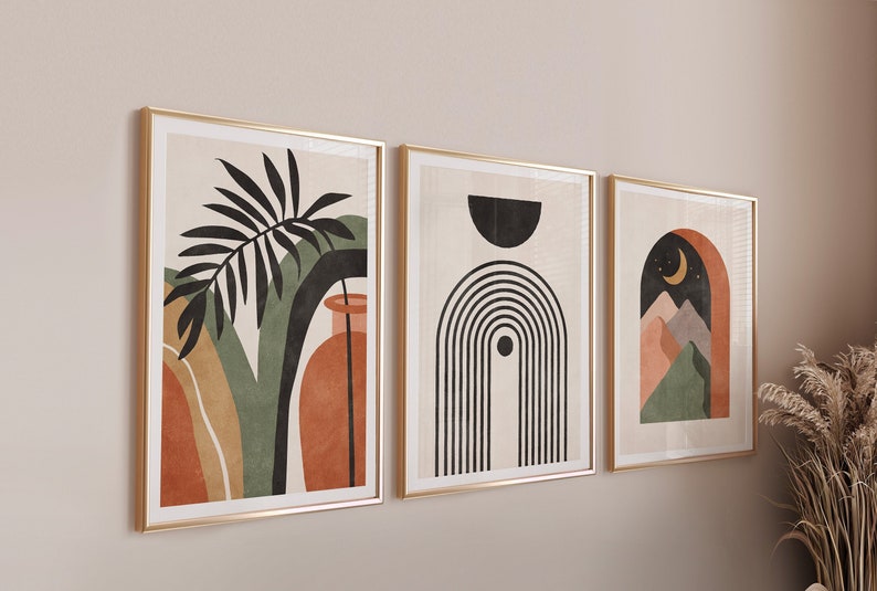 May include: Three framed abstract art prints with gold frames. The first print features a green and orange abstract design with a black palm leaf and a vase. The second print features a black and white abstract design with a rainbow and a circle. The third print features a green, orange, and brown abstract design with a crescent moon and mountains.