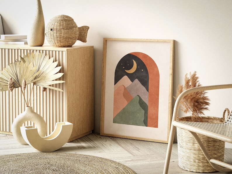 May include: A framed print with a modern abstract design featuring a crescent moon, stars, and mountains in shades of green, orange, and purple. The mountains are framed by a terracotta archway against a dark blue background.
