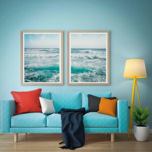 May include: Two framed ocean wave prints hang above a turquoise sofa with colorful pillows and a navy blue throw. A yellow floor lamp and a potted plant complete the room's decor, creating a coastal theme.