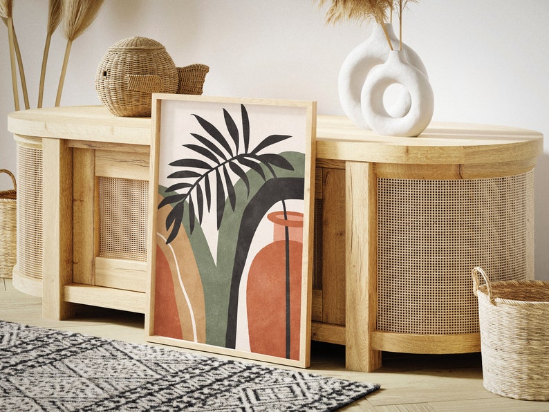 May include: A wooden cabinet with a woven rattan front and a large abstract art print featuring a green palm leaf and a red vase. The cabinet is decorated with a wicker basket and a white ceramic vase with a circular cutout.