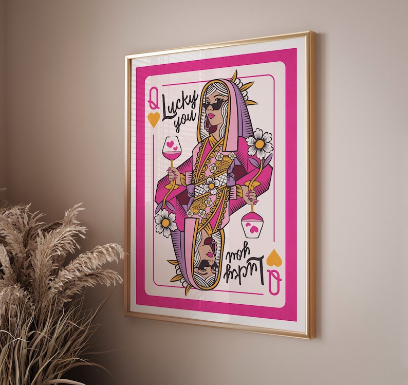 Puede incluir: Una carta de juego rosa con una reina sosteniendo una copa de vino. La carta dice "Lucky you" y "Queen of Hearts" en una fuente rosa y negra.