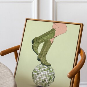 Pode incluir: Uma bota de cowboy verde e dourada com padr&atilde;o, equilibrada em cima de uma bola de discoteca prateada sobre um fundo verde claro.