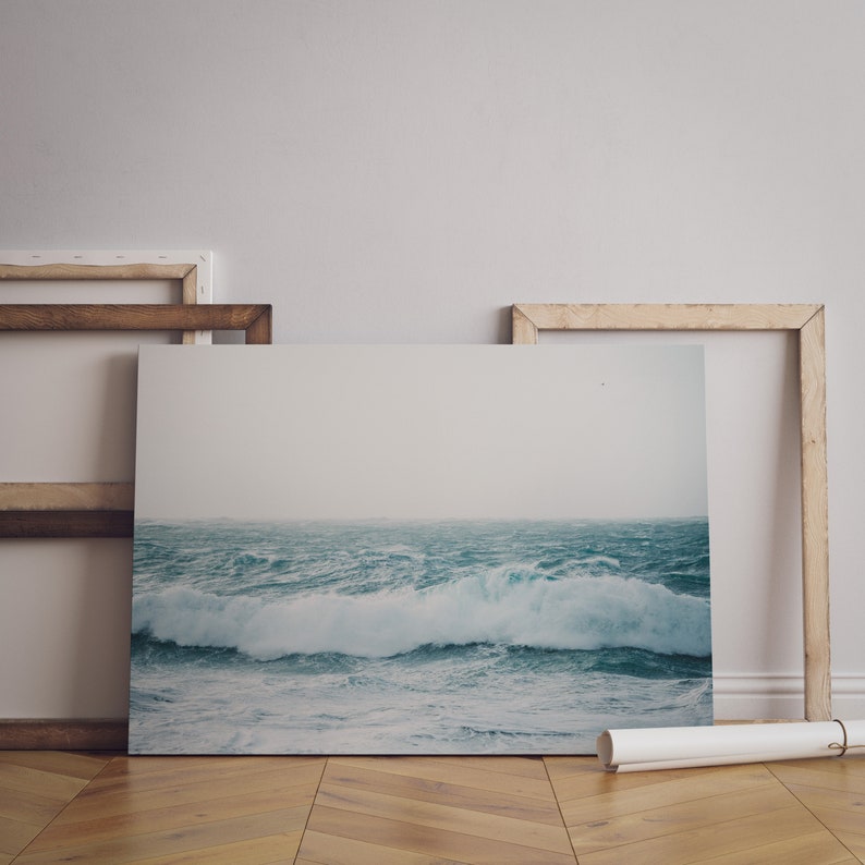 May include: A framed photograph of a stormy ocean scene with large waves crashing against the shore. The photograph is displayed on a wooden floor with a white wall in the background.