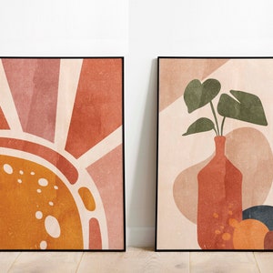 K&ouml;nnte beinhalten: Zwei gerahmte abstrakte Kunstdrucke im minimalistischen Stil. Der erste Druck zeigt eine stilisierte Sonne in Orange-, Gelb- und Rosat&ouml;nen. Der zweite Druck zeigt eine Vase mit einer Blattpflanze in Gr&uuml;n-, Braun- und Beiget&ouml;nen.