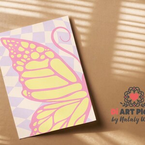May include: A print featuring a butterfly wing design in yellow and pink, set against a checkered background of light purple and white. The artwork is on a rectangular paper, with the artist's logo in the bottom right corner.