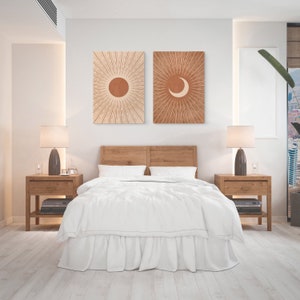 May include: A white bed with a wooden headboard and two nightstands with lamps. There are two framed prints on the wall above the headboard, one with a sun and one with a crescent moon.