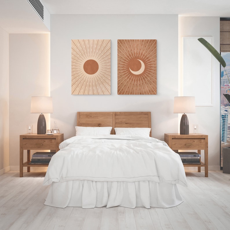 May include: A white bed with a wooden headboard and two nightstands with lamps. There are two framed prints on the wall above the headboard, one with a sun and one with a crescent moon.