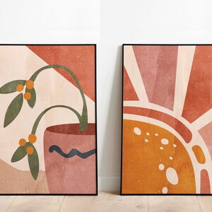 K&ouml;nnte beinhalten: Zwei abstrakte Kunstdrucke im minimalistischen Stil. Der Druck auf der linken Seite zeigt eine gr&uuml;ne Pflanze mit orangefarbenen Beeren in einem rosafarbenen Topf vor einem pfirsichfarbenen Hintergrund. Der Druck auf der rechten Seite zeigt eine stilisierte Sonne in den Farben Orange, Pfirsich und Wei&szlig; vor einem pfirsichfarbenen Hintergrund.
