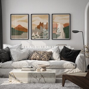 May include: Three abstract landscape prints in black frames hang above a white sofa with black and white throw pillows. A wooden chair with a woven seat sits in the corner of the room.