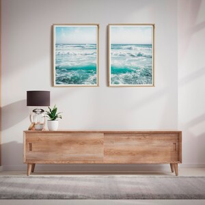 May include: Two framed ocean wave prints hang above a wooden cabinet with sliding doors. A black lamp, a small potted plant, and decorative items sit on the cabinet. A gray rug and pink curtain are also visible.