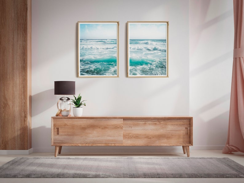 May include: Two framed ocean wave prints hang above a wooden cabinet with sliding doors. A black lamp, a small potted plant, and decorative items sit on the cabinet. A gray rug and pink curtain are also visible.