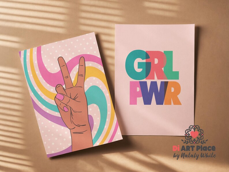 May include: Two art prints. One features a hand making a peace sign with a retro swirl background. The other print says "GRL PWR" in colorful block letters. Both prints are on a brown surface.