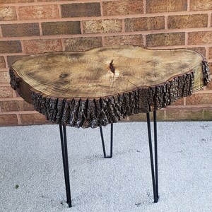 May include: A rustic wooden table with a live edge top and black hairpin legs. The table is made from a tree trunk slice and has a natural wood finish.