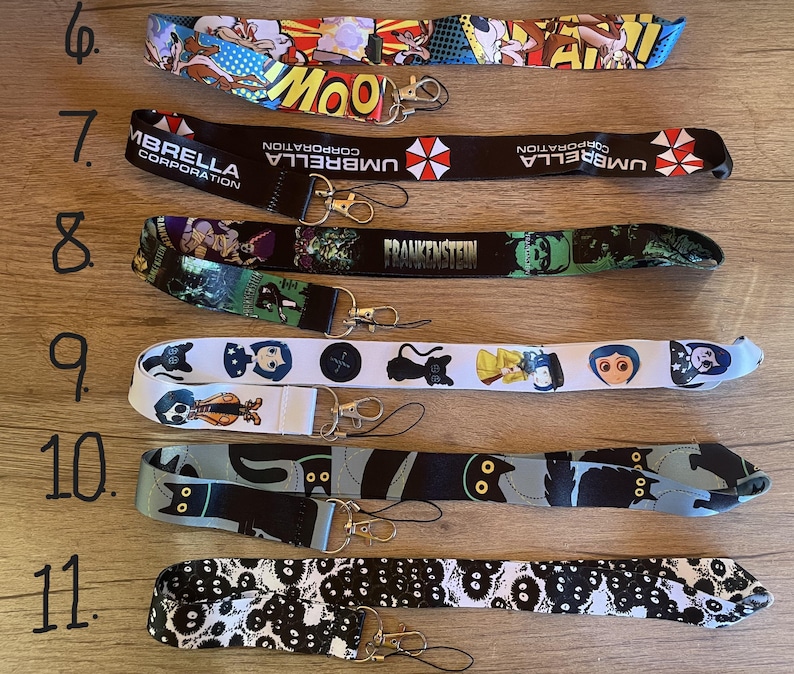 May include: Eleven different lanyard designs featuring various characters and logos. The lanyards are white, black, blue, and red with various graphic designs. The lanyards are numbered 6 through 11.