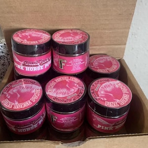 May include: A collection of small, pink and black jars with the text "PINK HORSE POWER" and "FLEE FARMS" printed on them. The jars are arranged inside a cardboard box. The lids feature a pink horse graphic.