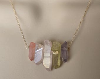 May include: A delicate necklace featuring a series of colorful crystal points. The crystals are arranged in a row, showcasing shades of pink, white, yellow, and purple. The necklace is suspended from a fine gold chain, creating an elegant and natural look.