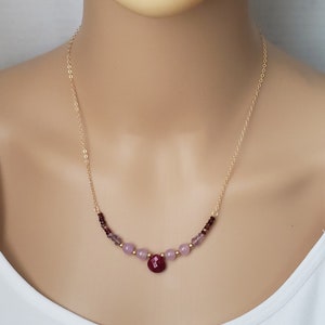 May include: A gold chain necklace with a red gemstone pendant and purple and pink beads.