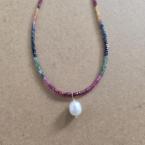 May include: A multi-coloured beaded necklace with a white pearl pendant. The necklace has small, faceted beads in blue, green, yellow, pink, and purple. The pearl hangs from a delicate gold-coloured wire.