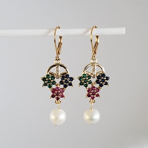 May include: Gold dangle earrings with a cluster of three flower-shaped charms set with green, blue, and pink gemstones. Each earring is topped with a pearl drop.